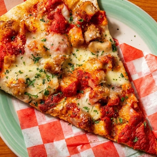 A slice of pizza with chicken, red sauce, melted cheese, and parsley on a plate.